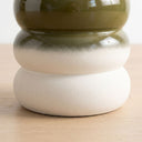 A close-up of the terra stool ceramic base with a stacked, rounded tiered design. The top section has a glossy olive green glaze, while the middle and bottom sections have a matte, textured off-white finish.