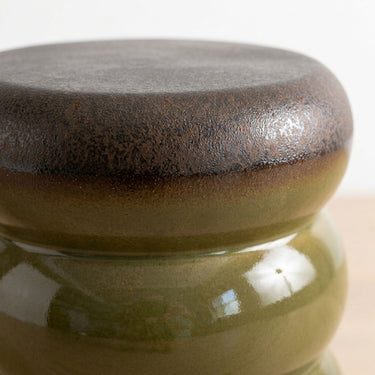 a ceramic stool close up view with a rounded top in a glossy olive green and dark brown glaze.