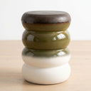A ceramic decorative stool with a stacked, rounded design. The top section features a dark brown glazed finish, followed by olive green, a white-to-light-gray gradient section, and a solid matte off-white base.