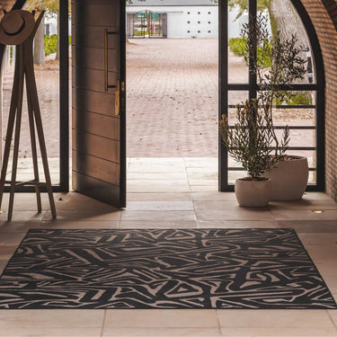 Area rug with an abstract black and beige geometric pattern, on a tiled entryway floor in front of open glass doors.