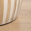 Close-up of he tulum side table top with vertical beige and cream stripes, resting on a light wood floor.