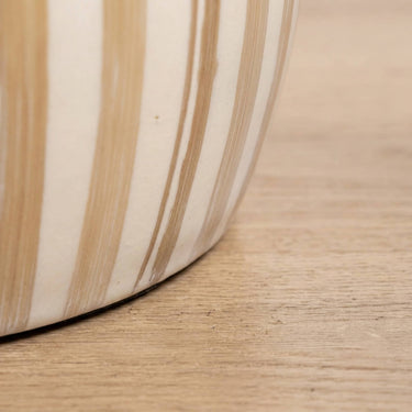 Close-up of he tulum side table top with vertical beige and cream stripes, resting on a light wood floor.