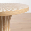 Close-up of a round mother of pearl side table with a sunburst inlay pattern on the tabletop and curved base, shown against a softly blurred light background.