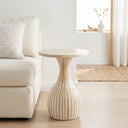 A round side table with a flared pedestal base, featuring vertical light mother or pearl  stripes, styled in a bright, modern living room next to a cream sofa.