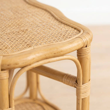 Close-up of a light natural rattan bed side table showing the woven cane seat, curved bamboo frame, and wrapped joints against a soft neutral background.