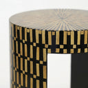 A close-up of a cylindrical side table featuring a black and natural bamboo geometric inlay pattern.