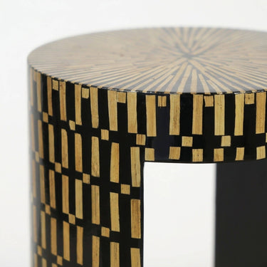 A close-up of a cylindrical side table featuring a black and natural bamboo geometric inlay pattern.