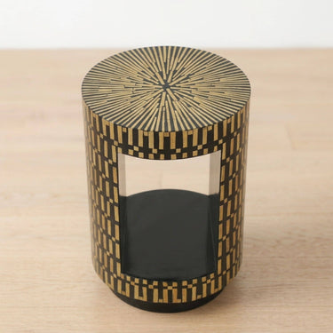 Round side table with a black and bamboo geometric patterned lacquer finish, featuring a opening on the front and a black base.