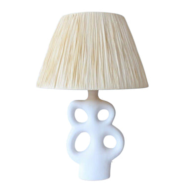White ceramic cut-out table lamp with a natural raffia drum shade.