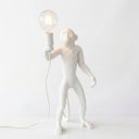 A white monkey figurine table lamp holding a clear glass bulb light, set against a plain white background.