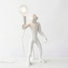 A white monkey figurine table lamp holding a clear glass bulb light, set against a plain white background.
