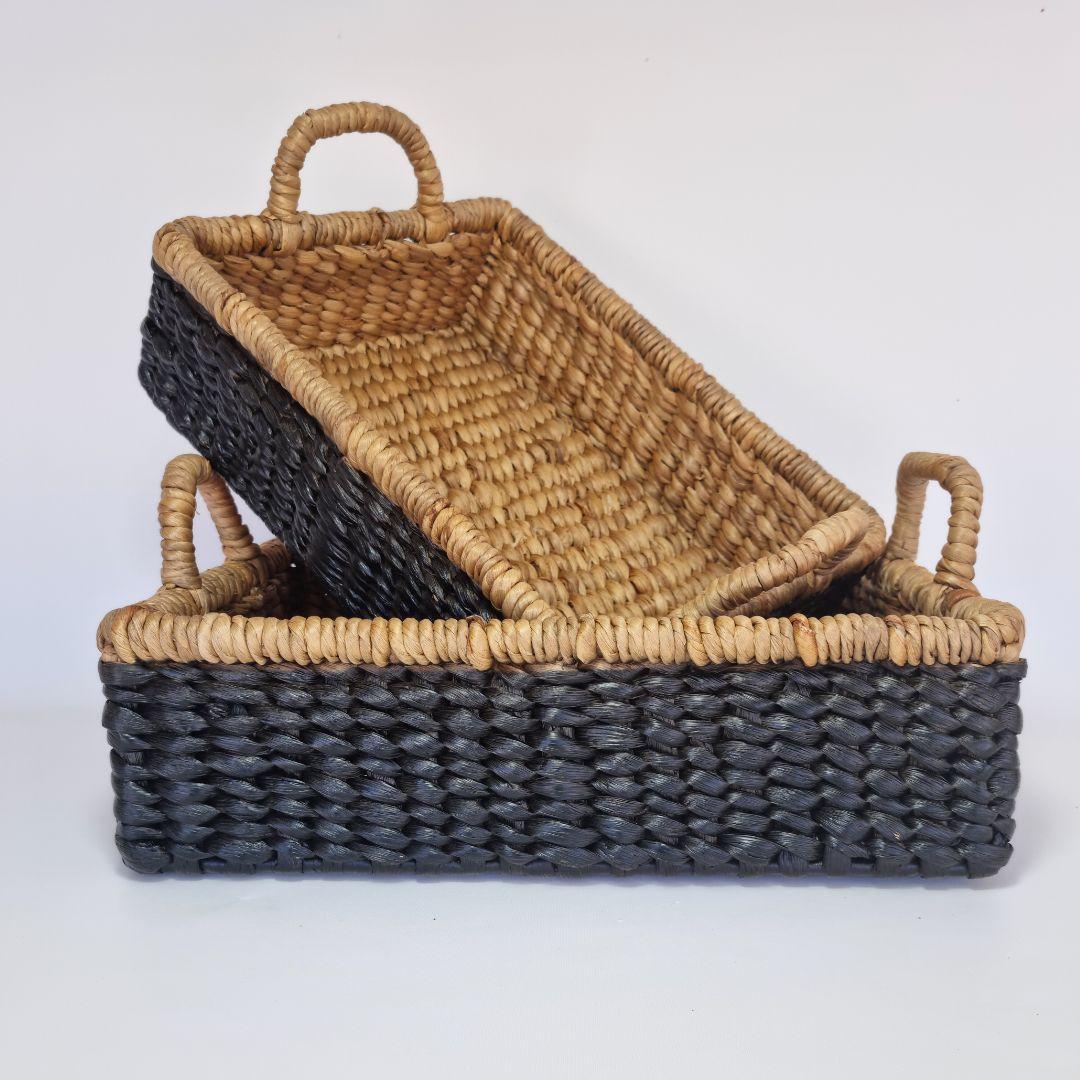 Woven basket trays styled simply on a surface, showing coordinated sizes and natural dark tones